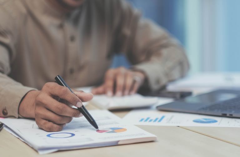 Pessoa com uma caneta na mão, checando informações em um gráfico.